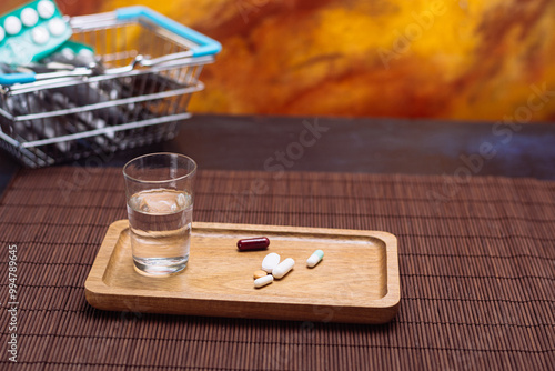 Assorted pills on wooden tray with water and shopping basket in background photo