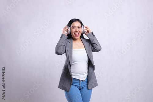 beautiful young office girl cheerful to camera holding and wearing headset headphone listening music wearing grey suit isolated on white background. lifestyle concept, entertainment, technology