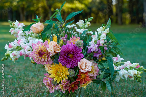 Large bouquet of freshly cut flowers. Glass vase sitting on the grass. Dahlia, lisianthus, snapdragons, starflowers, sage, bouquet, arrangement, outdoors