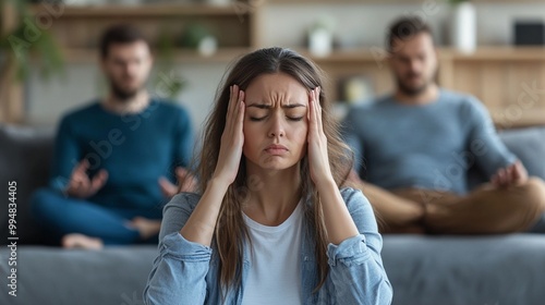 Stressed woman holding head in hands, sitting on couch between two men. Tense atmosphere in living room depicts family conflict or relationship troubles.