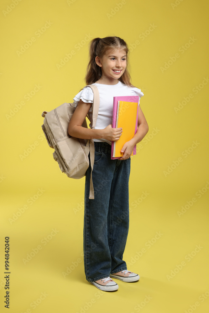 Positive girl with backpack and books on yellow background Positive girl with backpack and books on yellow background