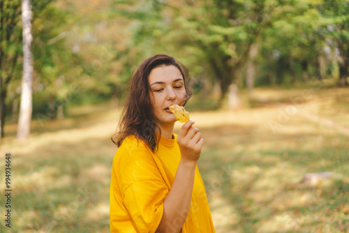 A woman enjoys a autumn day while playfully holding a yellow leaf