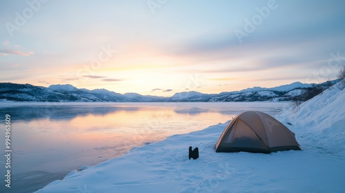 A lone tent on a snow-covered lakeshore with mountains in the distance at sunset