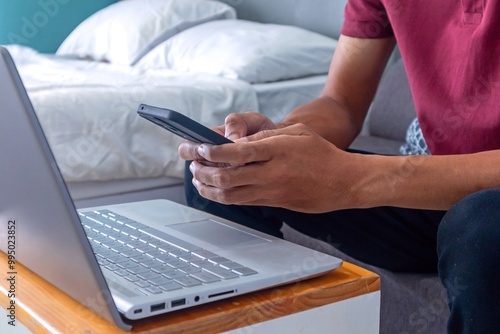 Man working in his bedroom with a smartphone and laptop. Working from home, working on holiday or working from anywhere concept.