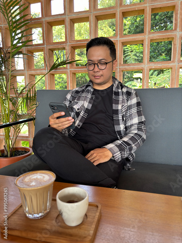 Man sitting relaxed in a cafe while holding a cellphone with coffee on the table