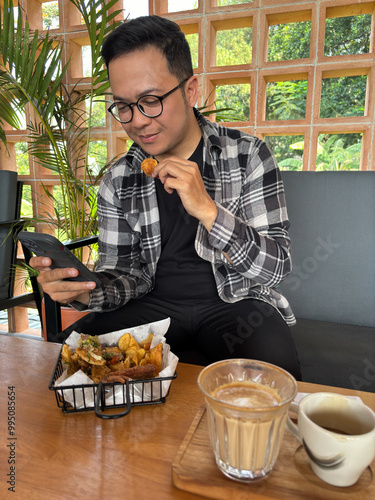 Man sitting in cafe looking at smartphone while eating snacks