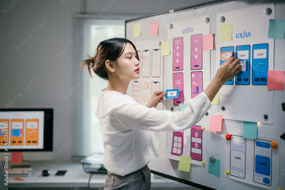 © Parichat - Young asian woman working as ux ui designer is designing a mobile application, using sticky notes on a whiteboard to create a user-friendly interface