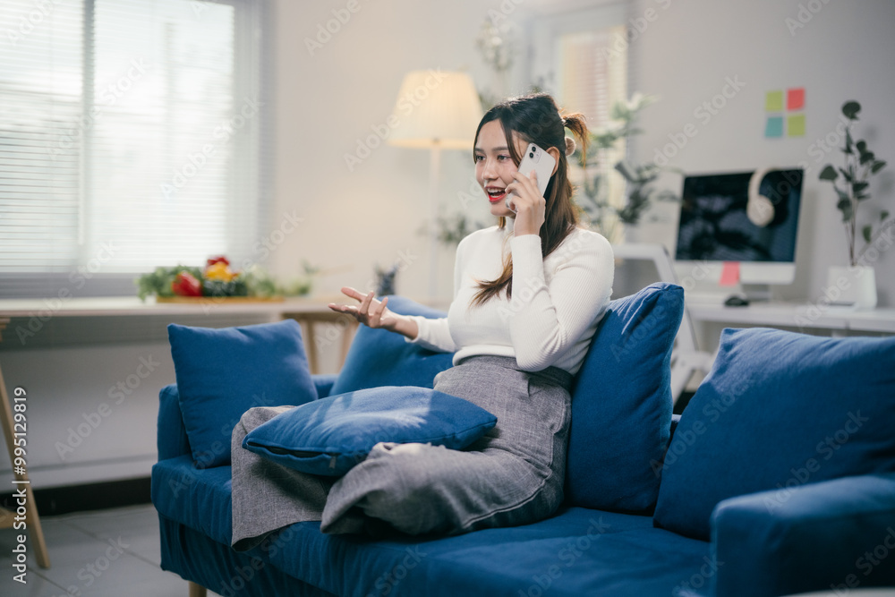 Obraz premium Young entrepreneur is working remotely and having a business call with her smartphone while relaxing on a comfortable sofa