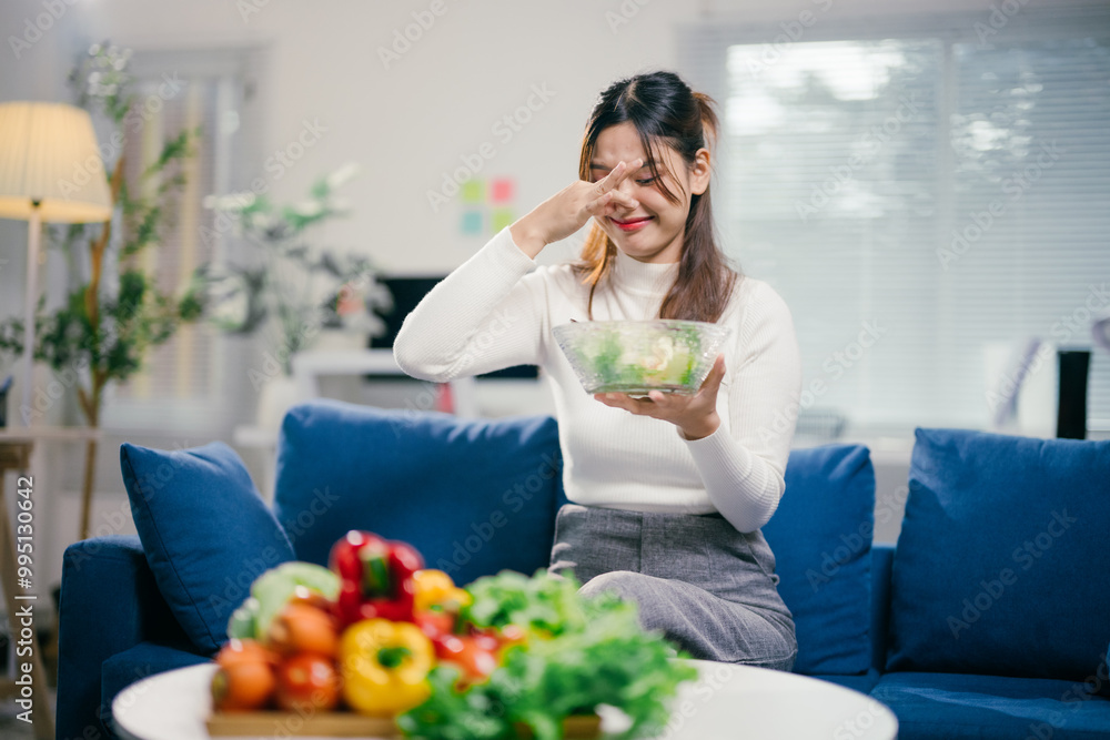 Young woman is holding a bowl of salad and pinching her nose closed with her fingers, showing her distaste for the healthy meal Young woman is holding a bowl of salad and pinching her nose closed with her fingers, showing her distaste for the healthy meal
