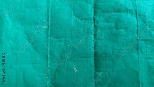 A close-up shot of a green fabric with creases and folds. The fabric has a textured appearance and a slightly faded color. It could be used for backgrounds, textures, or design elements.