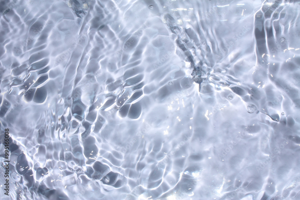 Bluewater waves on the surface ripples blurred. Defocus blurred transparent blue colored clear calm water surface texture with splash and bubbles. Water waves with shining pattern texture background. Bluewater waves on the surface ripples blurred. Defocus blurred transparent blue colored clear calm water surface texture with splash and bubbles. Water waves with shining pattern texture background.