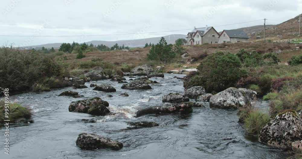 A tranquil river meanders through rocky areas and lush vegetation, with a quaint house nestled in the background under a cloudy sky in County Donegal. A tranquil river meanders through rocky areas and lush vegetation, with a quaint house nestled in the background under a cloudy sky in County Donegal.