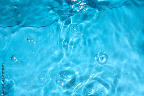 Blue water with ripples on the surface. Defocus blurred transparent blue colored clear calm water surface texture with splashes and bubbles. Water waves with shining pattern texture background.