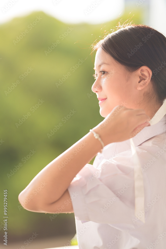 Portrait of long-haired Asian school girl wearing school presenter uniform tying a white, colorful bow on her head, standing in front of the classroom preparing for her final exam. Portrait of long-haired Asian school girl wearing school presenter uniform tying a white, colorful bow on her head, standing in front of the classroom preparing for her final exam.