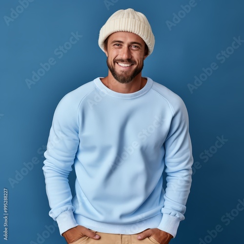 Happy man in a beige winter hat and a sweater. Portrait of a grown up man in a winter cap standing on a blue background looking at the camera. Cheerful young man in a pom pom hat. photo