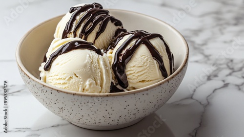 Three scoops of vanilla ice cream topped with chocolate sauce in a bowl on a marble background.
