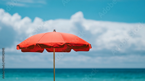 A vibrant red beach umbrella stands against a clear blue sky by the ocean in summer photo