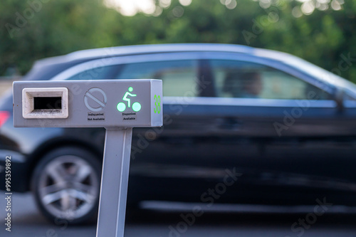 Bike-sharing station with availability indicator next to parked car on urban street