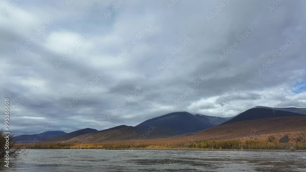Experience the tranquil beauty of a river as it moves past autumn-colored mountains, all under a shifting sky filled with dynamic clouds. Experience the tranquil beauty of a river as it moves past autumn-colored mountains, all under a shifting sky filled with dynamic clouds.
