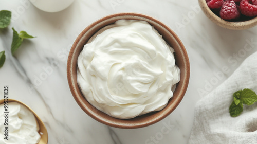 Creamy whipped topping in a bowl with fresh raspberries and mint on a marble countertop