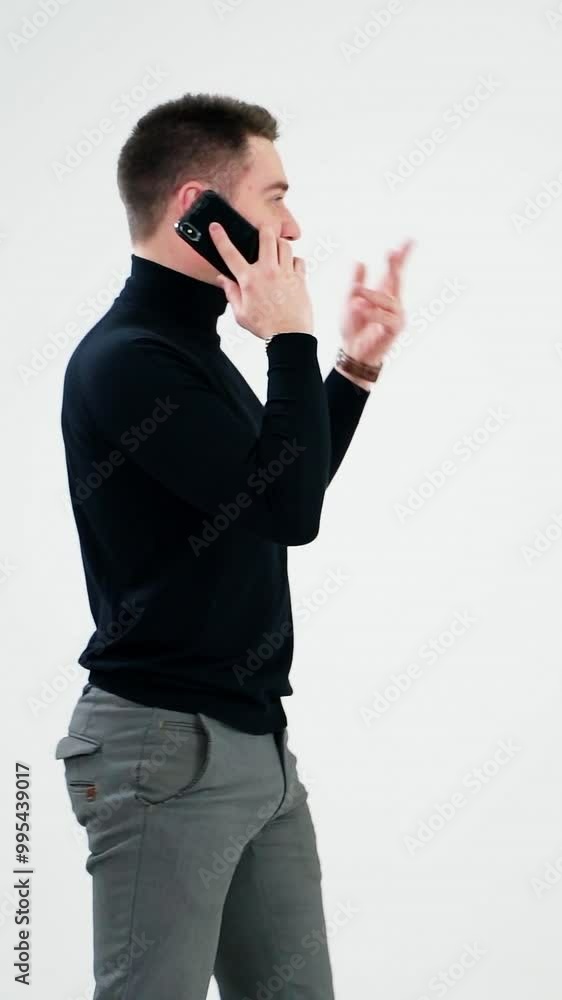 Young businessman talking on the phone. Handsome man in black sweater and grey trousers leading e-business through the cellphone. Man isolated on white. Vertical video Young businessman talking on the phone. Handsome man in black sweater and grey trousers leading e-business through the cellphone. Man isolated on white. Vertical video