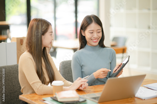 Two women work with tablets, work and chatting about paperwork and graphs.