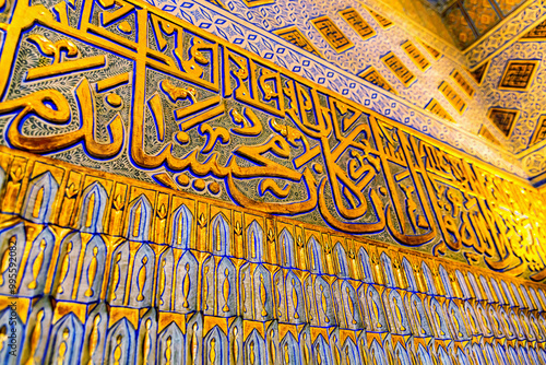 Close-up of ornate Islamic calligraphy in gold and blue hues on the wall of the Gur-e-Amir Mausoleum. Text in Arab language is fragment of Quran, sacred book for Muslims. Samarkand, Uzbekistan photo