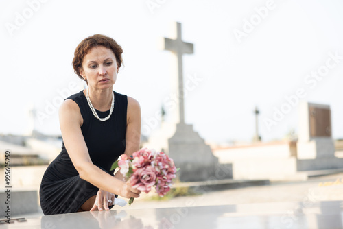 Фотография Grieving woman, dressed in black, placing bouquet of pink flowers on loved ones