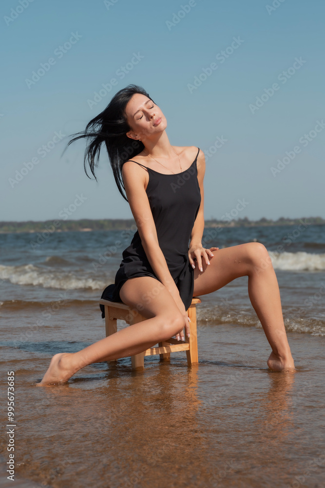 Young sexy beautiful woman is sitting on a chair in the sea and enjoying the bright rays of the sun. Young sexy beautiful woman is sitting on a chair in the sea and enjoying the bright rays of the sun.