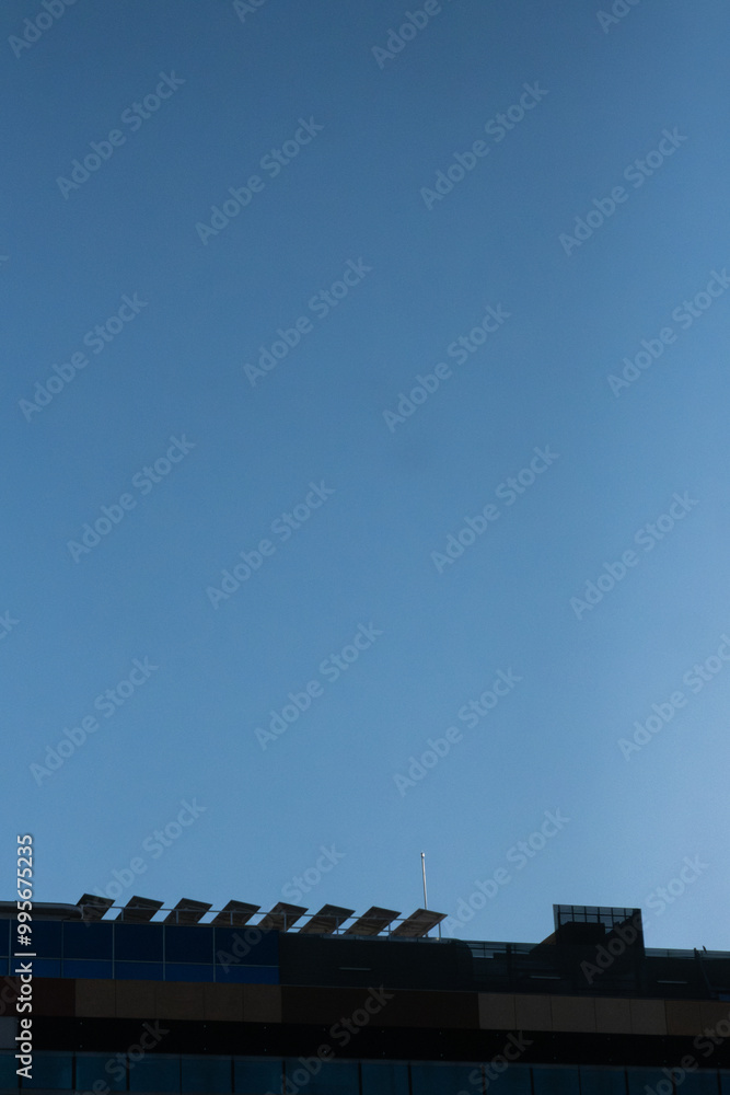 Backlit view of the roof of a modern office building with a photovoltaic solar panel installation on the community roof. Concept of decarbonization, sustainability and solar renewable energy Backlit view of the roof of a modern office building with a photovoltaic solar panel installation on the community roof. Concept of decarbonization, sustainability and solar renewable energy