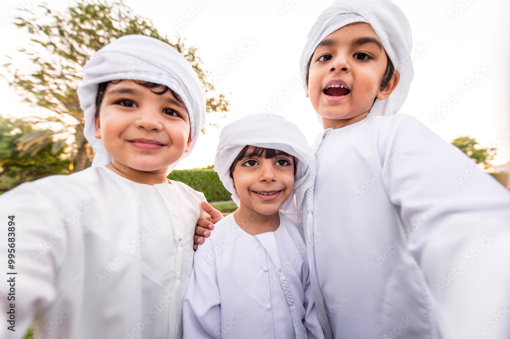 Children playing together in Dubai in the park. Group of kids wearing traditional kandura white dress from arab emirates Children playing together in Dubai in the park. Group of kids wearing traditional kandura white dress from arab emirates