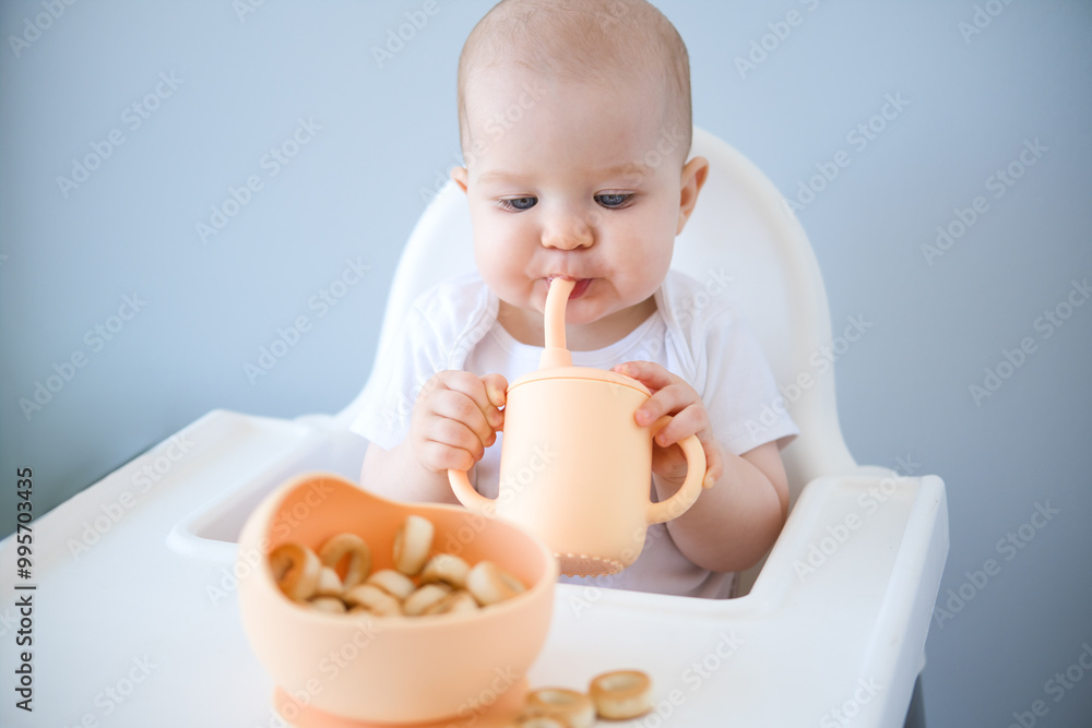 baby sitting in high chair, drinking clean water from baby sippy cup. weaning baby sitting in high chair, drinking clean water from baby sippy cup. weaning