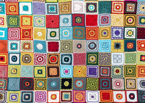 Top view of handmade multi colored plaid make from crochet granny squares with different motifs. Beautiful handicraft product for warm in wintertime.