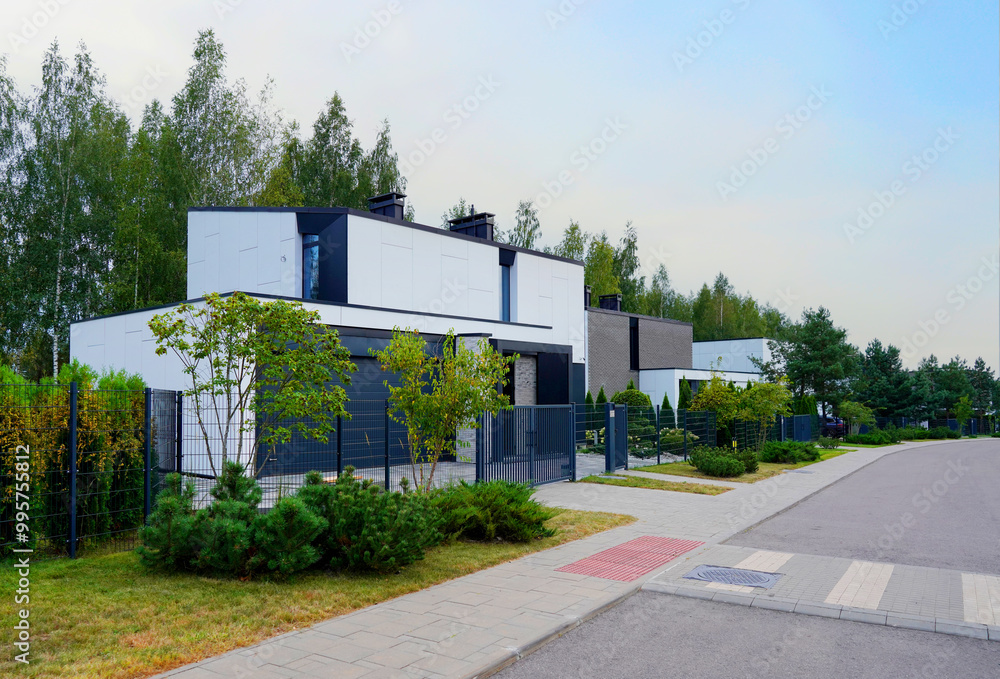 Obraz premium Prefab house. Street in residential area. Contemporary Residence in suburb. Rows of modern houses along road. Family house, Modern Home outside city. Trees, green lawn at Modern Villa.