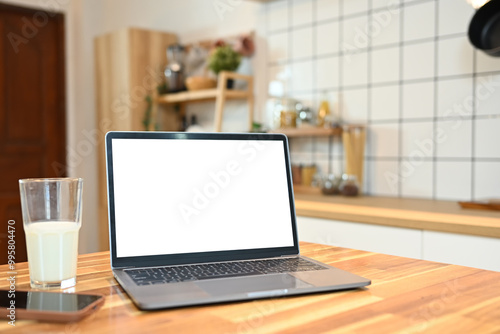 Close up shot of laptop with blank screen and a glass of milk on a wooden kitchen counter