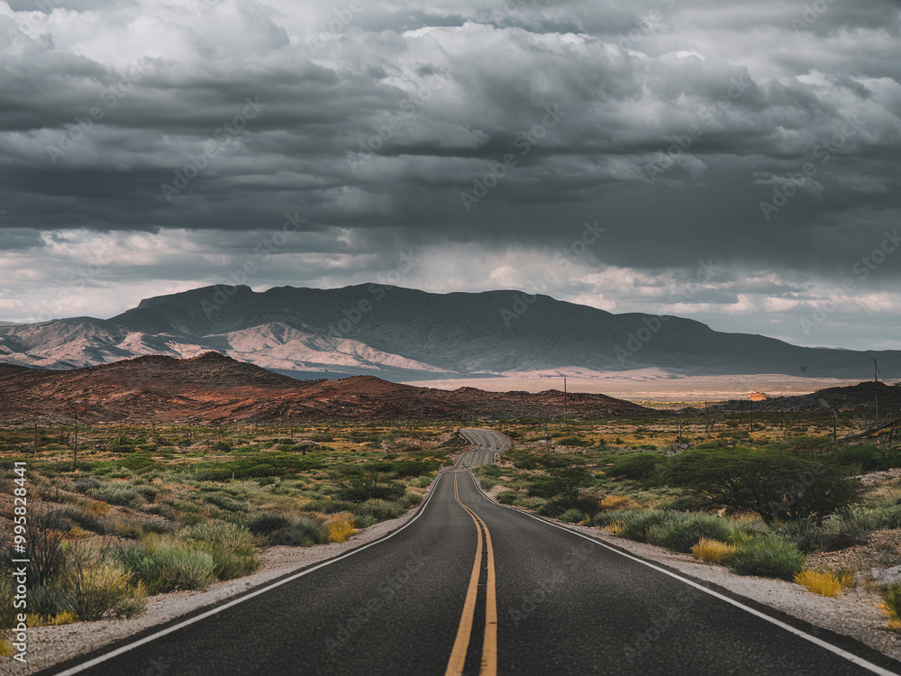 A winding road through arid desert landscape under dark clouds A winding road through arid desert landscape under dark clouds