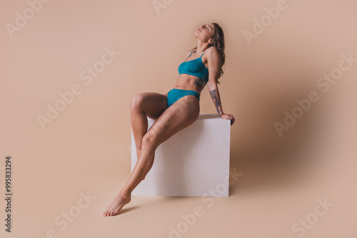 Full size photo of gorgeous young lady posing sit white cube wear cyan lingerie isolated beige background no retouch photo