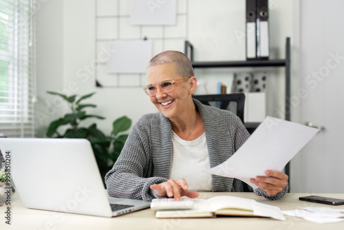 Senior Woman Working from Home on Laptop, Smiling and Holding Documents in Modern Home Office Setting