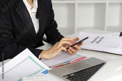 Business Professional Using Smartphone at Office Desk with Documents and Laptop