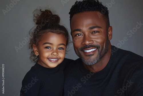 Mixed racial Father and cute daughter smiling and interacting in front of a plain background, dressed in simple clothes, captured in a family photo portrait shoot showcasing their joyful bond