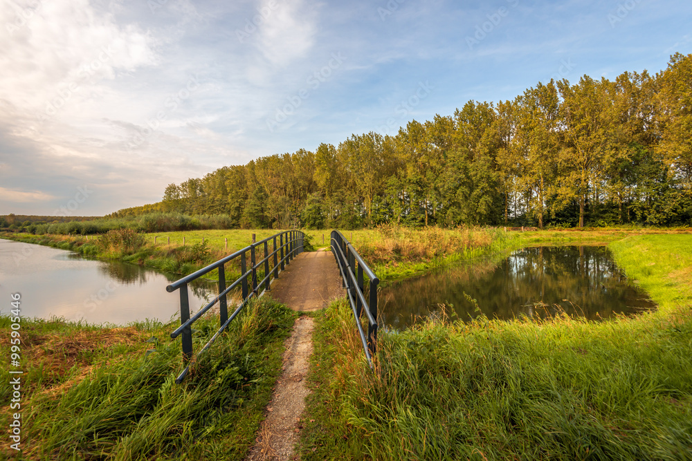 Bridge with iron railings over a small stream in a Dutch nature reserve. It is the last day of the summer season and the autumn colours are already visible.