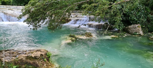 River flowing by stones between trees and small waterfall in the Sentierelsa Trail, Colle di Val d'Elsa, Italy. June 26, 2024. photo