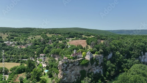 A breathtaking aerial view of a historic village nestled in lush green hills. The scene features a beautiful castle  on a cliffside, overlooking a river flowing through the valley. 