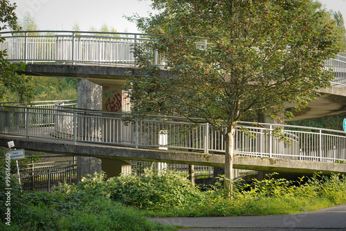 Side view of circular spiral bridge end. The grey concrete path spirals upwards between the green trees and bushes.  photo