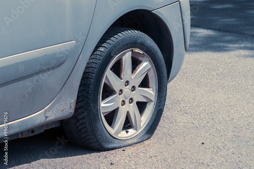 A car tire is flat and has a hole in it. The tire is on the side of the road