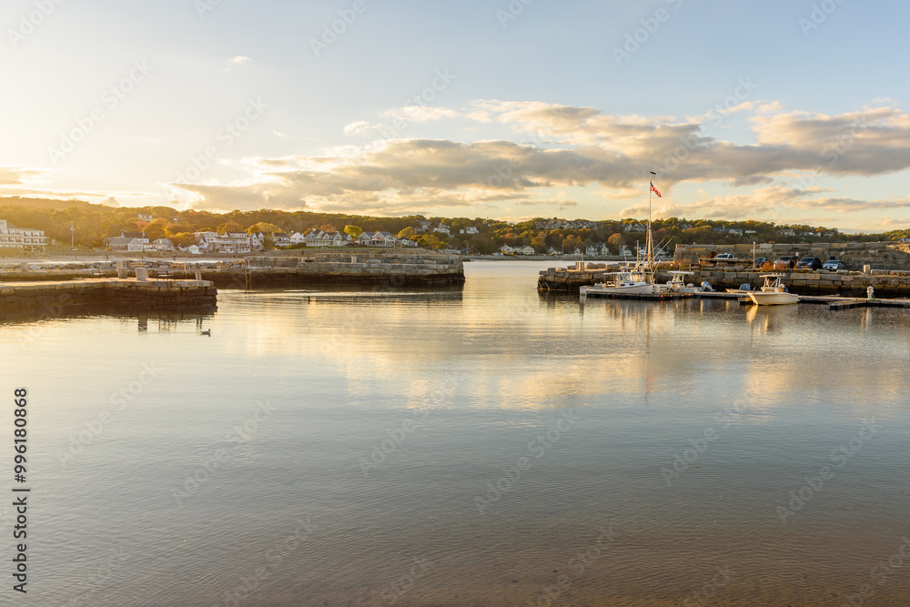 Empty harbour in a coastal town under clear sky at sunset in autumn. Houses among autumnal trees are visible in background. Empty harbour in a coastal town under clear sky at sunset in autumn. Houses among autumnal trees are visible in background.