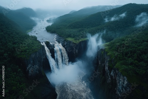The image captures a high angle view of a massive waterfall surrounded by mist and dense, green forest, showcasing the raw and unspoiled beauty of nature in exquisite detail.