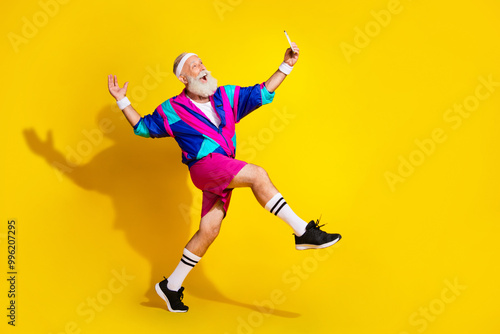 Full length photo of cheerful positive mature guy dressed retro sport jacket tacking selfie modern device emtpy space isolated yellow color background