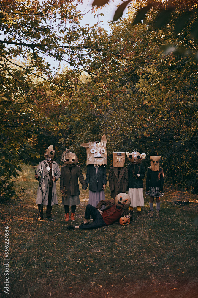 Terrifying gathering in forest. Seven figures in strange, handmade masks pose in golden light of autumn, casting bizarre spell on Halloween season. Concept of Halloween, spooky season, retro style. Terrifying gathering in forest. Seven figures in strange, handmade masks pose in golden light of autumn, casting bizarre spell on Halloween season. Concept of Halloween, spooky season, retro style.
