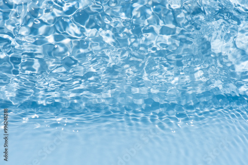 Blue water with ripples on the surface. Defocus blurred transparent blue colored clear calm water surface texture with splashes and bubbles. Water waves with shining pattern texture background.